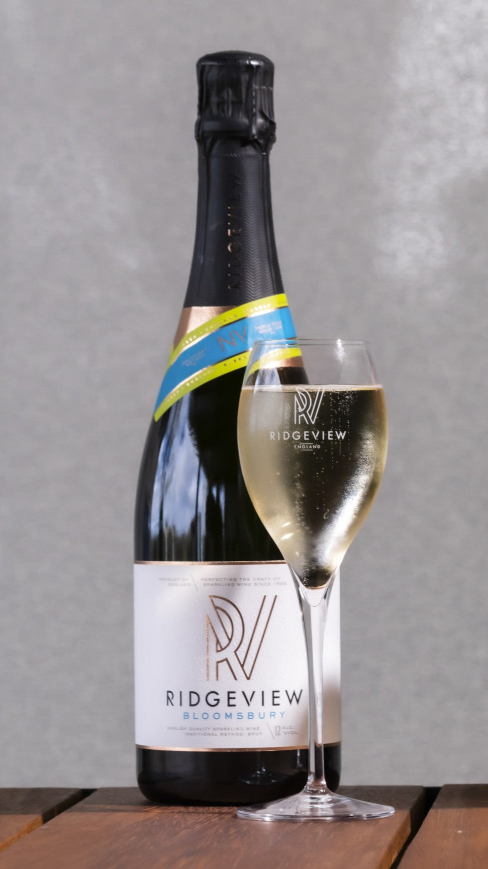 Bottle and glass of Ridgeview Bloomsbury sparkling wine on a wooden surface with a gray background