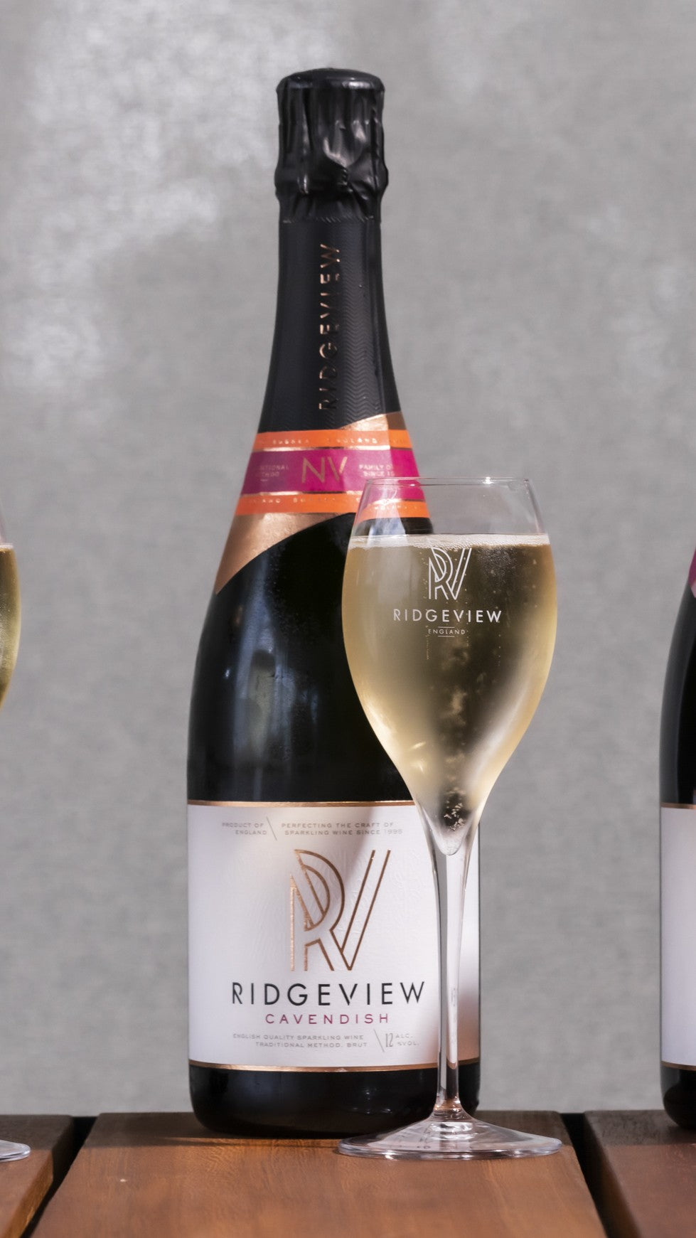 Ridgeview sparkling Cavendish wine bottle and glass on a wooden surface with a gray background